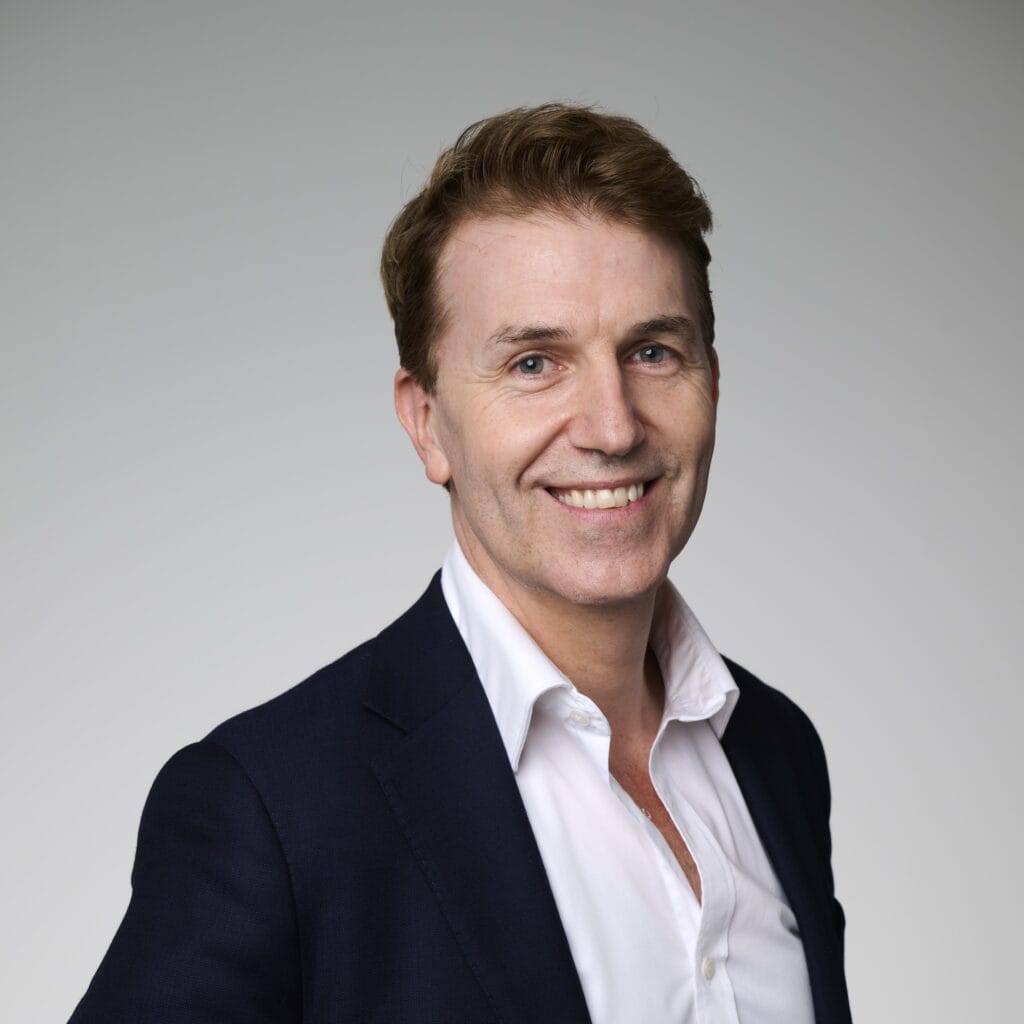 A corporate headshot of David Sly, smiling and wearing black and white clothing.
